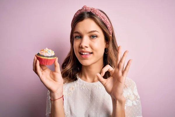 若いですブロンド女の子食べるA甘いですチョコレートカップケーキ以上ピンク隔離された背景行いますOk Signとともに指 優れたシンボル — ストック写真