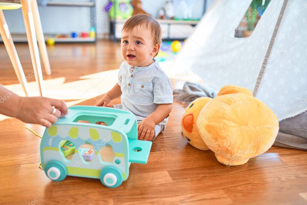 Adorable toddler sitting on the floor playing with toys at kindergarten