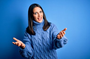 Mavi gözlü genç esmer kadın balıkçı yaka kazak giyiyor neşeli gülümseyerek yardım eli uzatıyor ve kabul görüyor..