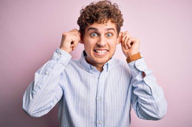 Sarışın, kıvırcık saçlı, beyaz arka planda çizgili tişört giyen, parmaklarıyla kulaklarını çekerek gülümseyen, komik hareketler yapan genç bir adam. Seçme sorunu