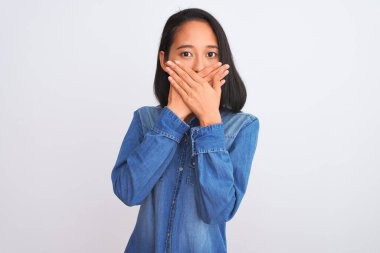 İzole edilmiş beyaz arka planda duran kot gömlek giyen genç ve güzel Çinli kadın yanlışlıkla ağızlarını kapatarak şok geçirdi. Gizli konsept.