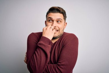 Mavi gözlü genç adam izole edilmiş arka planda dikiliyor. Ağzı tırnak yiyen eller üzerinde stresli ve gergin görünüyor. Endişe sorunu.