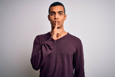 Beyaz arka plan üzerine gündelik süveter giyen genç ve yakışıklı Afro-Amerikan adam sessiz olup dudaklarını öpmek istiyor. Sessizlik ve gizli konsept.
