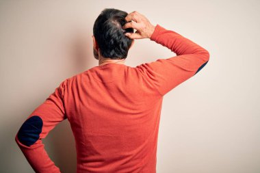 Orta yaşlı, turuncu süveter giyen, izole edilmiş beyaz arka planda duran, elleri kafasında şüpheyi düşünen, orta yaşlı bir adam.