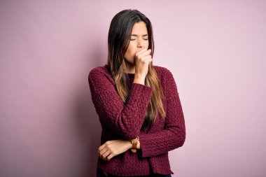 İzole edilmiş pembe arka plan üzerine günlük süveter giyen genç ve güzel bir kız kendini iyi hissetmiyor ve soğuk algınlığı veya bronşitin belirtisi olarak öksürüyor. Sağlık hizmeti kavramı.