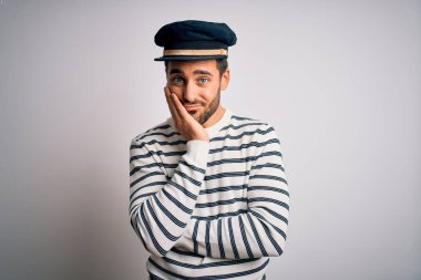 Sakallı, denizci üniformalı ve kaptan şapkalı genç yakışıklı adam kollarını kavuşturup depresyondan sıkılmış ve yorgun görünüyor..