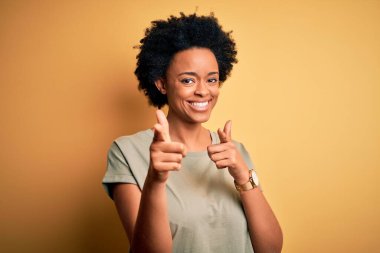 Kıvırcık saçlı, sıradan tişörtlü, neşeli ve komik yüzlü genç ve güzel Afro-Amerikan kadın kamerayı işaret ediyor. İyi enerji ve titreşimler.