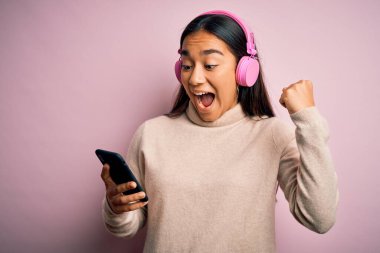 Genç, güzel Asyalı bir kadın müzik dinliyor. Akıllı telefon ve kulaklık kullanıyor. Gururla bağırıyor, zaferi ve başarıyı kutluyor.