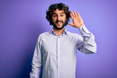 Mor arka planda duran sakallı yakışıklı iş adamı. Mutlu ve güler yüzlü, dostça bir jest yapıyor.