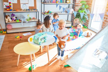 Güzel öğretmen ve bir grup çocuk anaokulunda bir sürü oyuncakla oynuyorlar.