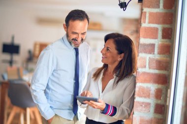 Mutlu ve kendinden emin gülümseyen iki orta yaşlı iş adamı. Ofiste tablet kullanarak birlikte çalışmak, gülümsemek.