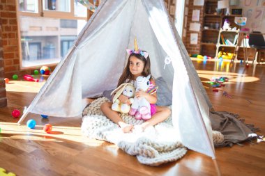 Anaokulunda Tip 'in içinde yerde oturan sevimli çocuk bir sürü oyuncağın etrafında oturuyor.