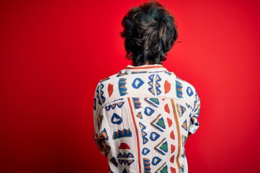 Tatilde olan yakışıklı bir adam, yaz tişörtü giyip izole edilmiş kırmızı arka plan üzerinde geriye bakıyor ve çapraz kollarla diğer tarafa bakıyor.