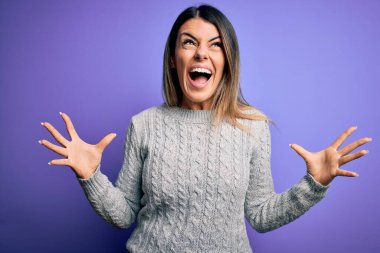 İzole edilmiş mor arka plan üzerinde duran sıradan bir süveter giyen genç ve güzel bir kadın çılgın ve sinirli bir şekilde bağırıyor ve agresif bir ifade ve kollarla bağırıyor. Hayal kırıklığı konsepti.