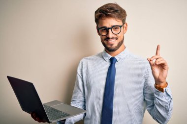 Gözlüklü genç işadamı beyaz arka planda duran dizüstü bilgisayarını kullanarak çalışıyor. Bir fikir ya da soru işareti ile şaşkın bir şekilde mutlu bir yüzü işaret ediyor.