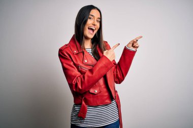 Genç, güzel, esmer, sıradan çizgili tişört ve kırmızı ceket giyen, gülümseyen ve kameraya bakan iki eliyle ve parmaklarıyla yüzünü gösteren bir kadın..