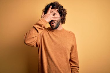 Sakallı, sıradan bir süveter giyen, sarı arka planda duran, yüzü ve gözleri kapalı, utangaç bir ifadeyle parmaklarından bakan genç yakışıklı bir adam..