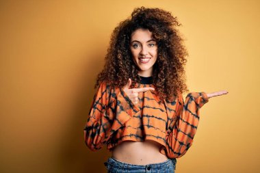 Kıvırcık saçlı ve piercingli genç ve güzel bir kadın. Sıradan bir tişört giyiyor. Hayret ediyor ve kameraya gülümsüyor..