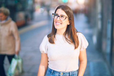 Mutlu ve kendinden emin gülümseyen genç ve güzel bir kadın. Kasaba caddesinde yüzünde gülümsemeyle dikilirken