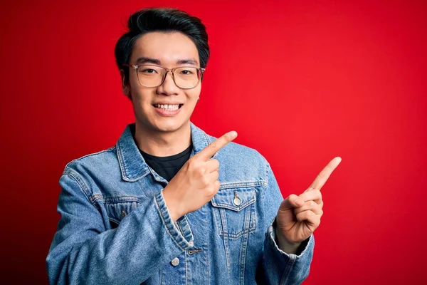 Nuori Komea Kiinalainen Mies Yllään Farkkutakki Lasit Punaisella Taustalla Hymyillen — kuvapankkivalokuva