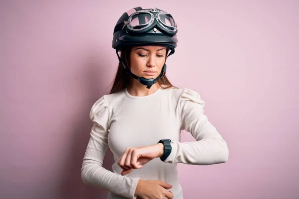 若いです美しいですオートバイの女性とともに青い目ピンクの背景の上に元ヘルメットを身に着けています手首の時計で時間をチェック リラックスして自信 — ストック写真