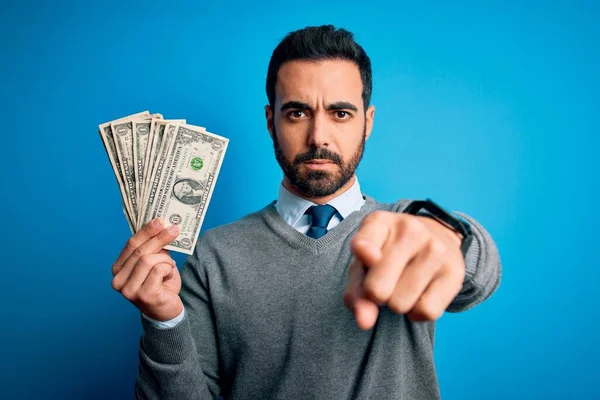 年轻英俊的男人留着胡子 蓝色背景上握着一堆钞票 手指指向相机和你 正面是积极自信的手势 — 图库照片