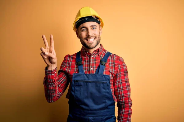 年轻的建筑工人身穿建筑制服 头戴安全帽 头戴黄色的隔离背景 带着自信和快乐的笑容 用手指指了指二号 — 图库照片