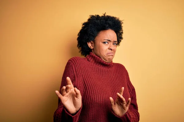 Young beautiful African American afro woman with curly hair wearing casual turtleneck sweater disgusted expression, displeased and fearful doing disgust face because aversion reaction.