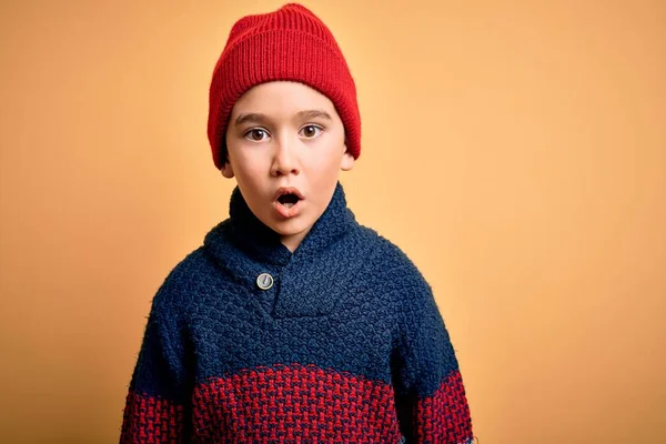 若いです男の子身に着けているウールキャップと冬のセーター以上黄色隔離された背景恐怖とショックで驚きの表情 恐怖と興奮した顔 — ストック写真