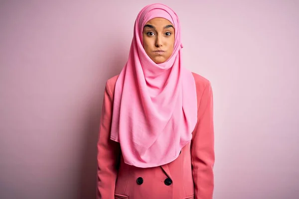 ピンクのイスラム教徒のヒジャーブとビジネスジャケットを身に着けている若い美しいブルネットのビジネスマンの女性は面白い顔で頬をパフ 口は空気で膨脹し 狂気の表現 — ストック写真
