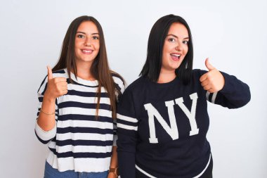 İzole edilmiş beyaz arka plan üzerinde sıradan kıyafetler giyen genç ve güzel kadınlar mutlu bir el hareketi yapıyorlar. Kameraya bakıp başarıyı gösteren ifade onaylanıyor.