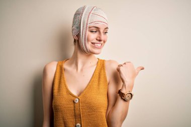 Genç, güzel, kızıl saçlı, kazara yaralanmış, kafasında bandajla gülümseyen, gülümseyen ve baş parmağıyla yüzünü gösteren bir kadın..