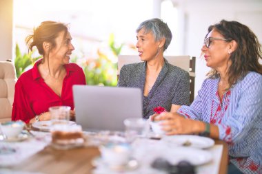 Orta yaşlı kadınlarla buluşup, öğle yemeği yiyip, kahve içiyorlar. Olgun arkadaşlar, güneşli bir günde evde dizüstü bilgisayar kullanarak mutlu bir şekilde gülümserler.