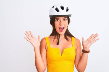 Bisiklet kaskı takan genç güzel bisikletçi kız izole edilmiş beyaz arka planda mutlu ve heyecanlı duruyor. Kazanan ifade zaferi büyük bir gülümsemeyle kutluyor ve ellerini kaldırıyor.