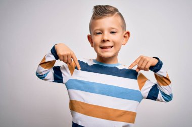 Mavi gözlü küçük beyaz çocuk izole edilmiş arka planda çizgili tişört giyiyor. Yüzünde bir gülümsemeyle, gururlu ve mutlu bir şekilde kendini işaret ediyor..