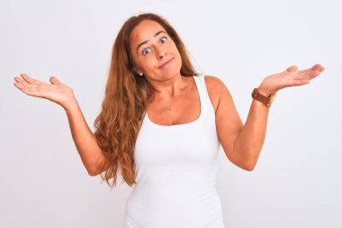 Orta yaşlı olgun bir kadın, beyaz soyutlanmış arka planda duruyor. Kolları ve elleri havada, kafası karışmış bir ifade. Şüphe kavramı.