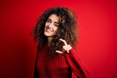 Kıvırcık saçlı, normal kırmızı kazak giyen, gülümseyen, kendine güvenen, el hareketi yapan, küçük beden işareti yapan ve kameraya bakan genç ve güzel bir kadın. Ölçü kavramı.