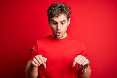 Sarışın, kıvırcık saçlı, kırmızı arka planda sıradan tişörtler giyen, reklam veren, şaşırmış yüzlü ve ağzı açık genç bir adam.