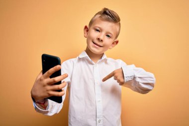 Küçük beyaz çocuk akıllı telefon kullanıyor ve ekranda kendini işaret eden sürpriz yüzüyle telefona bakıyor.