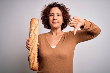 Orta yaşlı kıvırcık saçlı kadın izole edilmiş beyaz arka planda taze ekmek tutuyor. Kızgın yüzü var. Eksi işareti var.