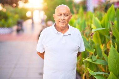 Kıdemli yakışıklı adam mutlu ve kendinden emin gülümsüyor. Kasaba caddesinde yüzünde gülümsemeyle dikilirken