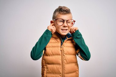 Mavi gözlü küçük beyaz çocuk, yüksek sesli müzik sesi için kulaklarını parmaklarıyla kapatan parlak gözlükler takıyor. Sağır kavramı.