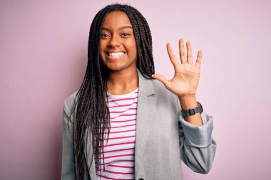 Genç Afro-Amerikan iş kadını pembe izole edilmiş arka planda duruyor ve beş numarayı işaret ediyor kendinden emin ve mutlu gülümserken..