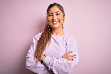 Pembe izole edilmiş arka plan üzerine kazak giyen genç ve güzel spor kadın kameraya bakarken kollarını kavuşturup gülümsüyor. Pozitif kişi.