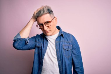 Genç, yakışıklı, gözlüklü ve kot ceketli bir adam pembe izole edilmiş arka plan kafa karıştırıcı ve soru hakkında merak uyandırıcı. Şüpheyle kararsız, kafa kafaya düşünerek. Düşünceli kavram.