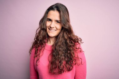 Kıvırcık saçlı, izole pembe arka planda günlük süveter giyen mutlu ve havalı bir gülümsemesi olan genç bir kadın. Şanslı kişi..