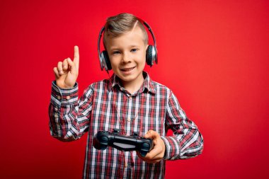 Küçük beyaz çocuk oyun oynuyor. Oyun sahası joystick 'ini kırmızı arka planda kullanıyor. Bir fikir ya da soru işareti ile şaşırıyor.