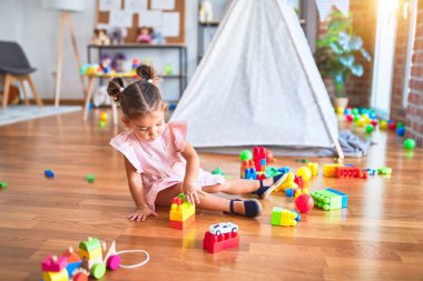 Genç ve güzel bir çocuk yerde oturmuş kreşteki yapı taşlarıyla oynuyor.