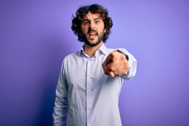Mor arka plan üzerinde duran sakallı yakışıklı iş adamı kameraya kızgın ve sinirli olduğunu gösteriyor.