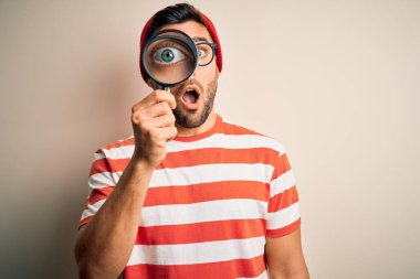 Genç dedektif arka plandaki izole edilmiş büyüteçten bakıyor. Şaşırmış bir yüzle korkmuş ve korku ifadesiyle heyecanlanmış.